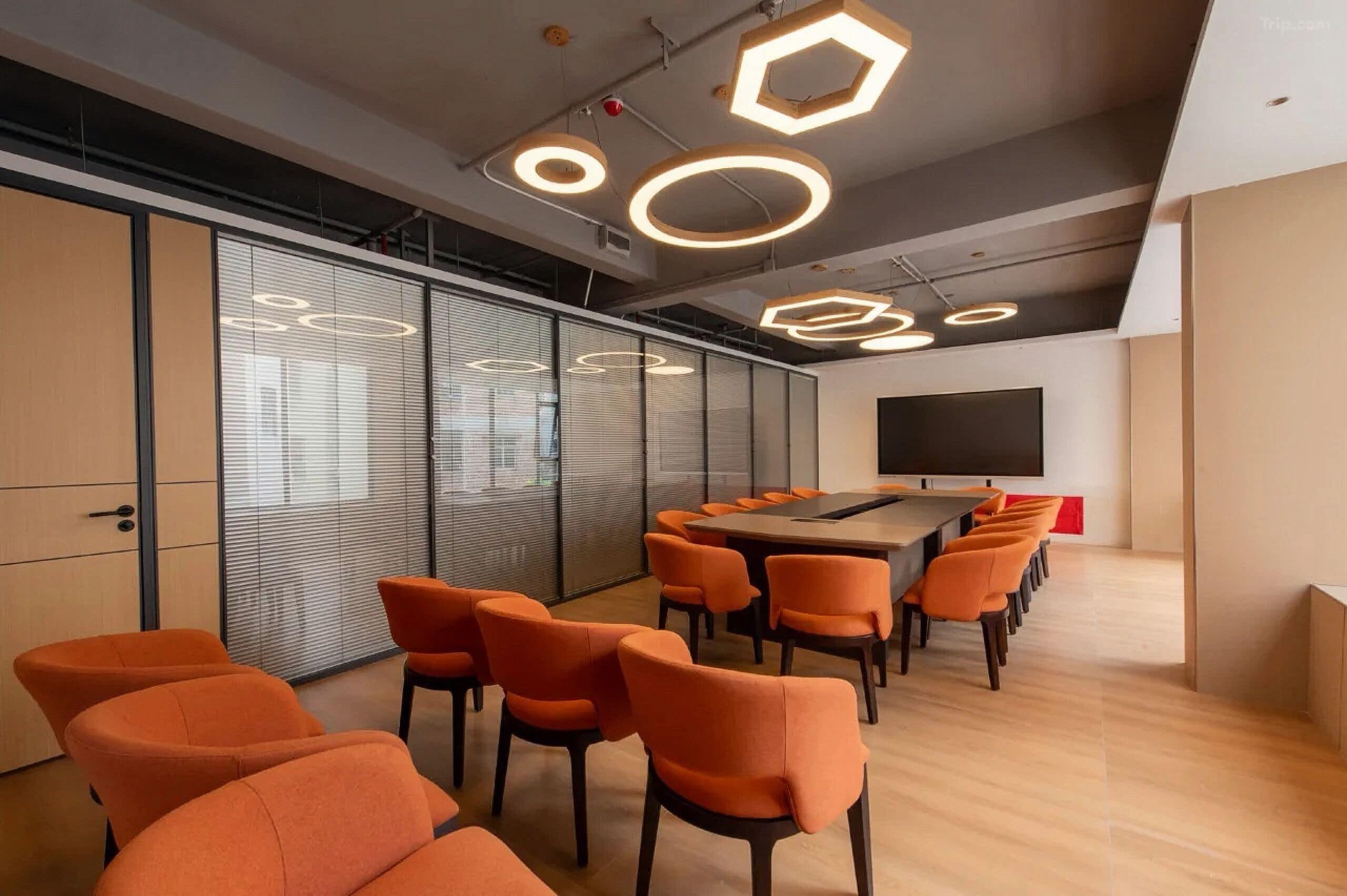A conference room with a long table, orange chairs, and hexagonal ceiling lights.