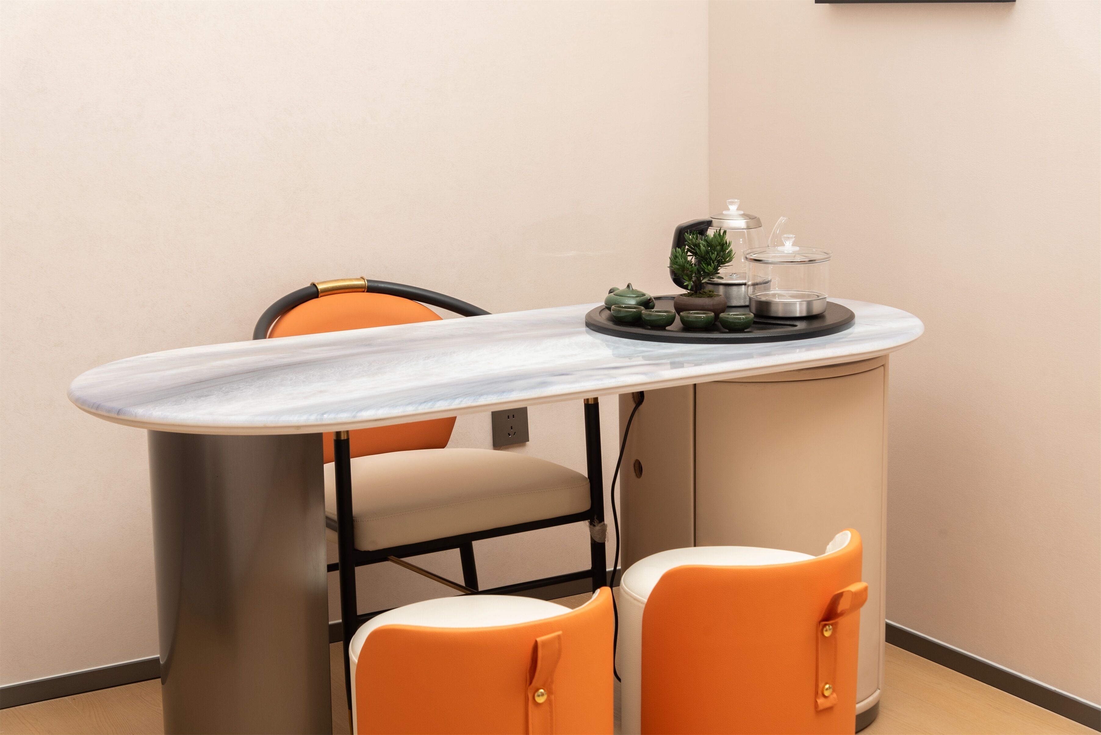 Un petit coin repas avec une table en marbre, deux chaises orange, une petite plante en pot et un meuble avec un plateau en verre.
