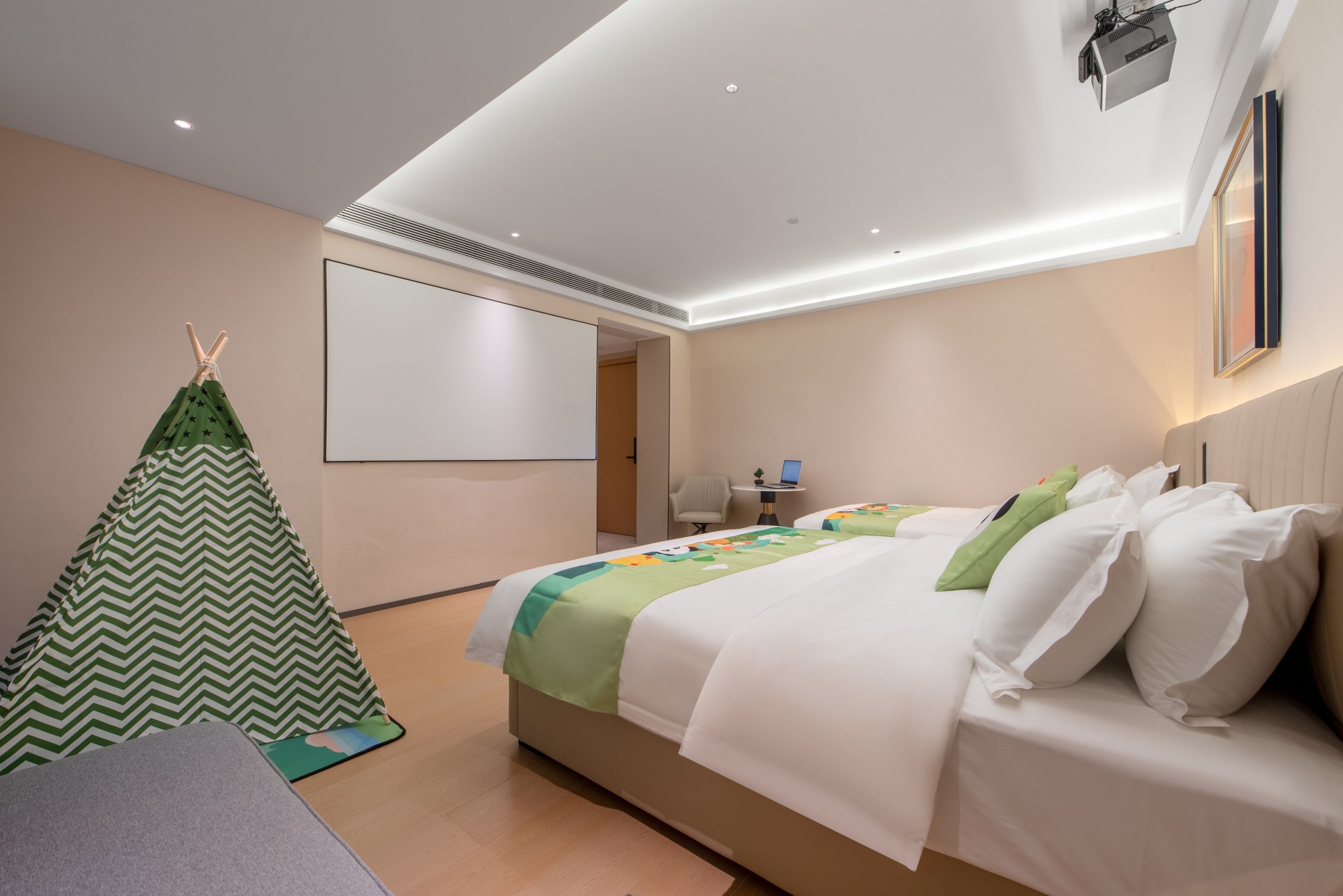 Une chambre d’hôtel avec un lit, un écran de projection, une petite table et une structure verte ressemblant à une tente.