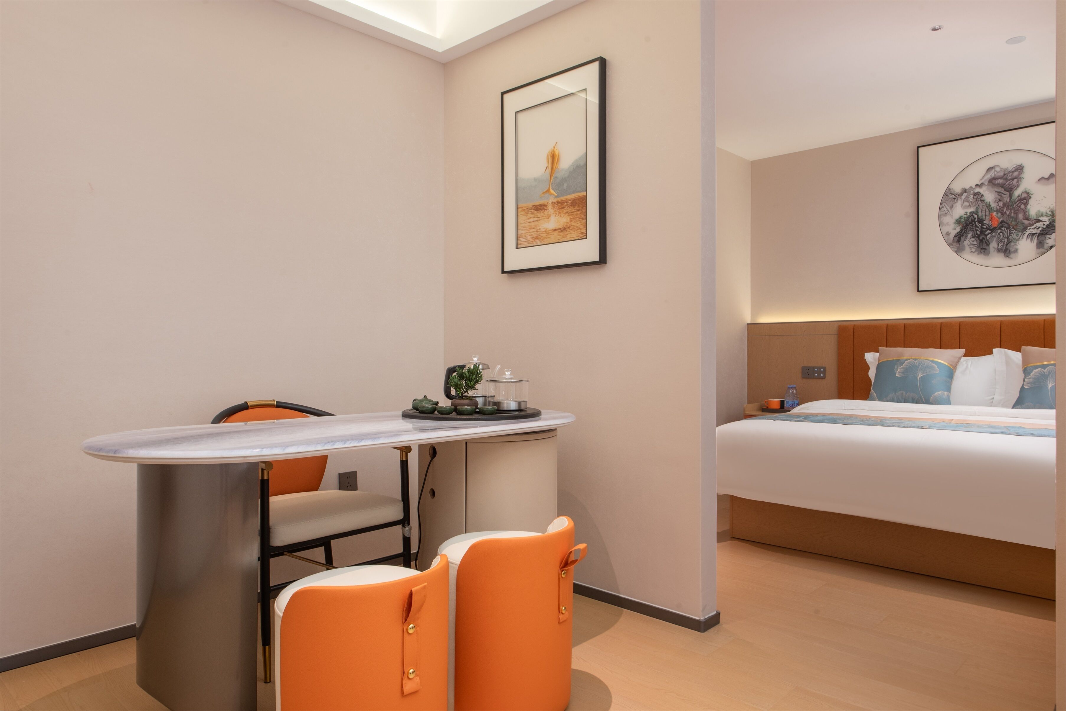 A hotel room with a bed, a dining table with chairs, a small kitchen area, and artwork on the walls.