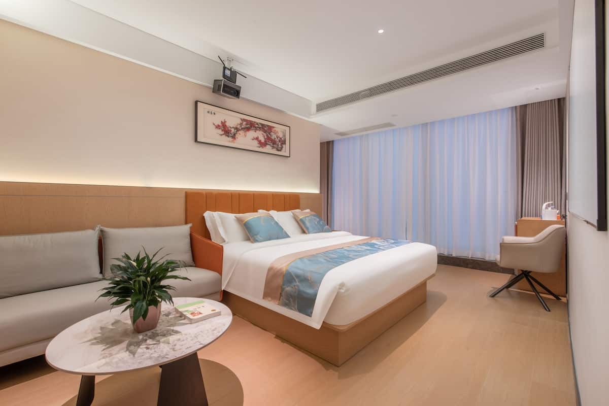 Ein modernes Hotelzimmer mit Bett, Sofa, Couchtisch und einer Topfpflanze.