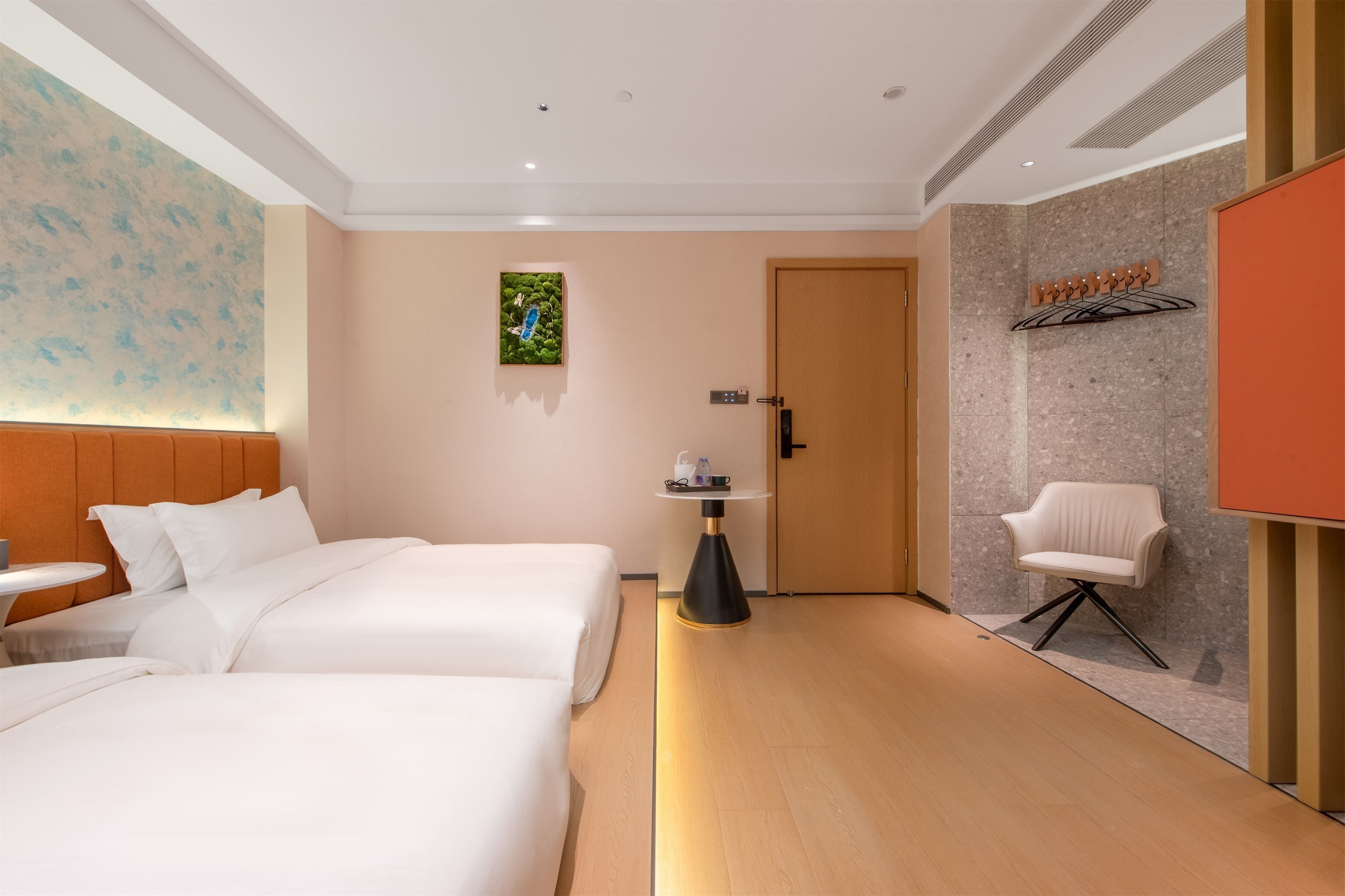 A hotel room with two beds, a small table, a chair, a coat rack, and a door.