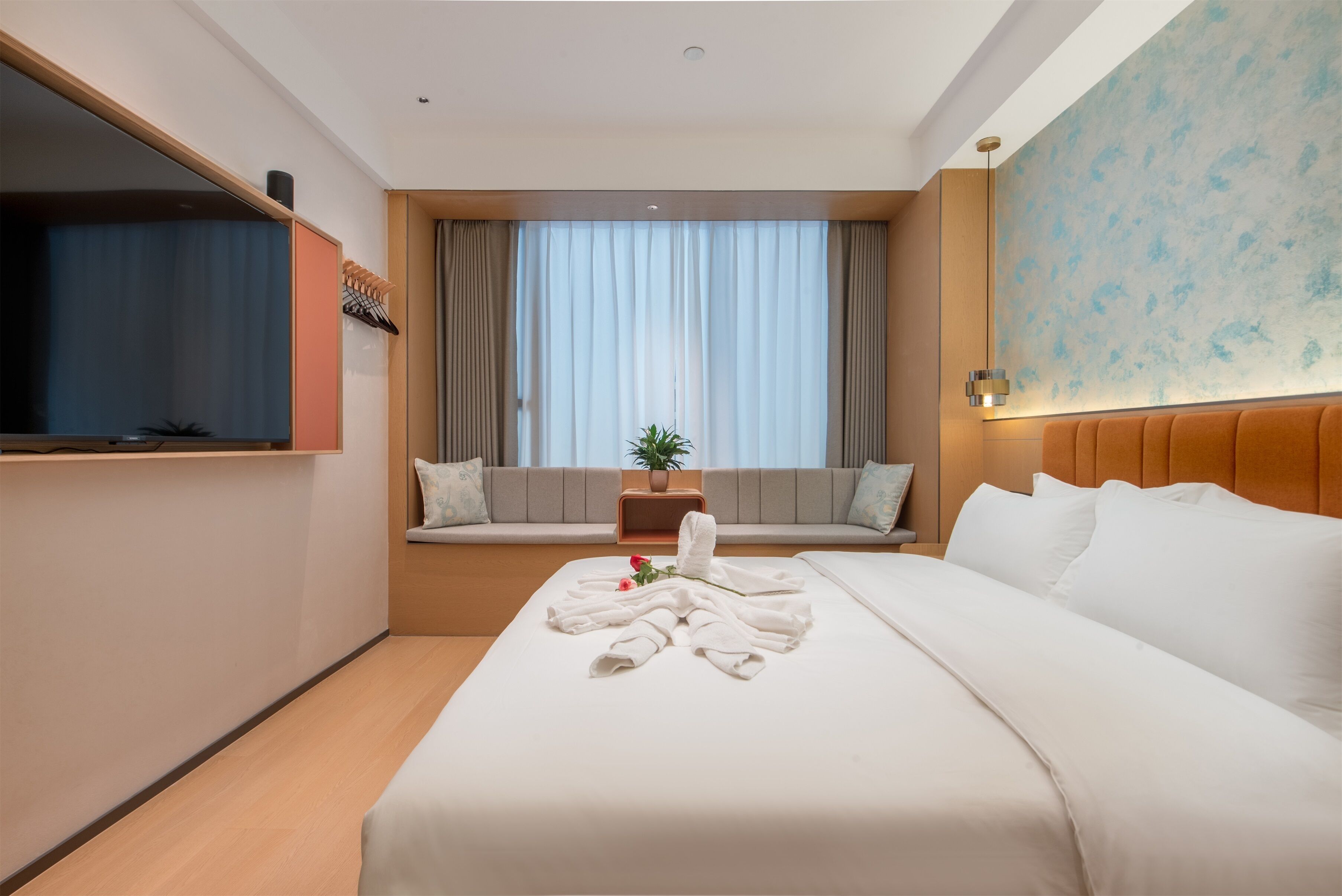 Hotelkamer met een bed, een televisie, een raam met gordijnen, een bank en een wand met een structuur.