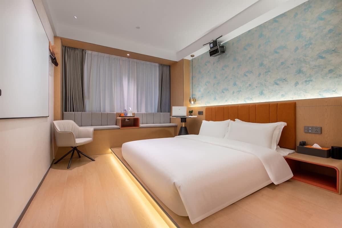Ein modernes Hotelzimmer mit einem großen Bett, einem Schreibtisch, einem Sessel und einem Fenster mit Vorhängen.