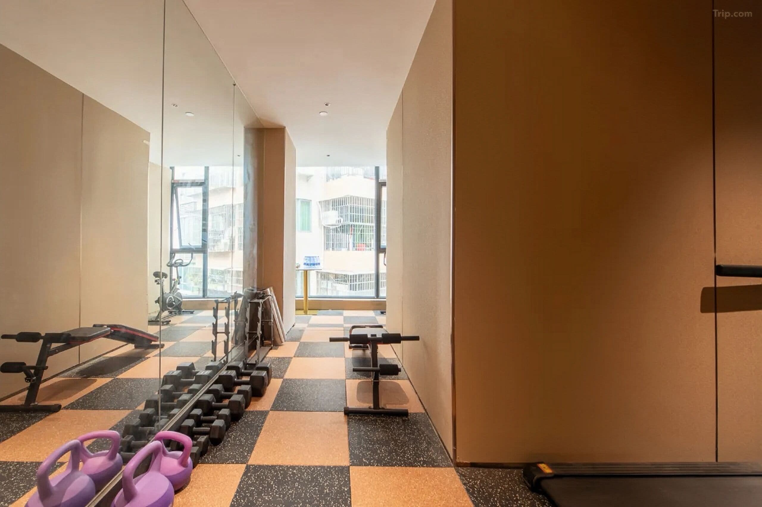 A gym with exercise equipment, a checkered floor, and a view of buildings through large windows.