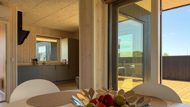 Une cuisine moderne avec des meubles en bois, une grande fenêtre et un coin repas agrémenté d’un panier de fruits.