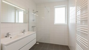 A modern bathroom with a large mirror, two sinks, a shower, and a window. - Apartment in Zoutelande Near Sunny Beach (Zoutelande)