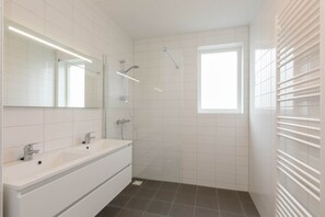 Ein modernes Badezimmer mit großem Spiegel, zwei Waschbecken, einer Dusche und einem Fenster.