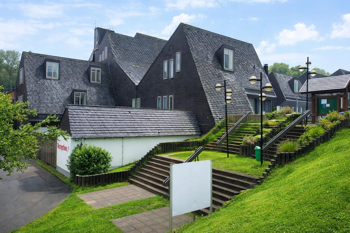 Ein Wohngebäude mit steilem Satteldach, einer kleinen Rezeption und einer Treppe zum Eingang.