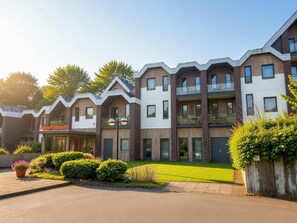 Ein modernes Mehrfamilienhaus mit Ziegel- und weißen Fassaden, Balkonen und einem gepflegten Rasen.