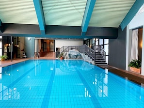 Ein Hallenbad mit gefliestem Boden, einer Treppe mit Geländer und Blick ins Innere.