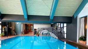 Una piscina interior con suelo de baldosas, una escalera con barandilla y vistas al interior.