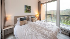 Un dormitorio con una cama grande, un cuadro, dos lámparas de noche y vistas a un balcón.