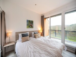 A bedroom with a large bed, a painting, two bedside lamps, and a view of a balcony. - Hambachtal Forest Hideaway Boutique Resort (Oberhambach)