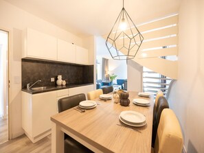 A modern kitchen with white cabinets, a black countertop, and a dining area with a wooden table set for four. - Hambachtal Forest Hideaway Boutique Resort (Oberhambach)