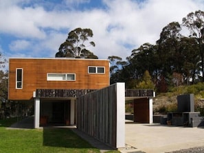 Un edificio moderno su due piani, con facciata in legno, ingresso coperto e un vialetto in cemento che conduce all'ingresso.