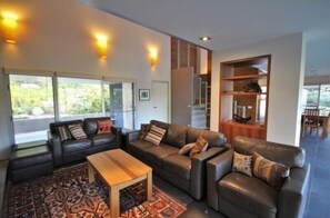 A modern living room with leather sofas, a wooden coffee table, and a large window with a view of greenery.