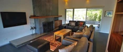 A modern living room with a fireplace, a large sofa, a coffee table, and a flat-screen TV mounted on the wall.