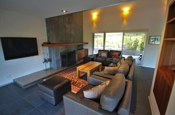 A modern living room with a fireplace, a large sofa, a coffee table, and a flat-screen TV mounted on the wall.