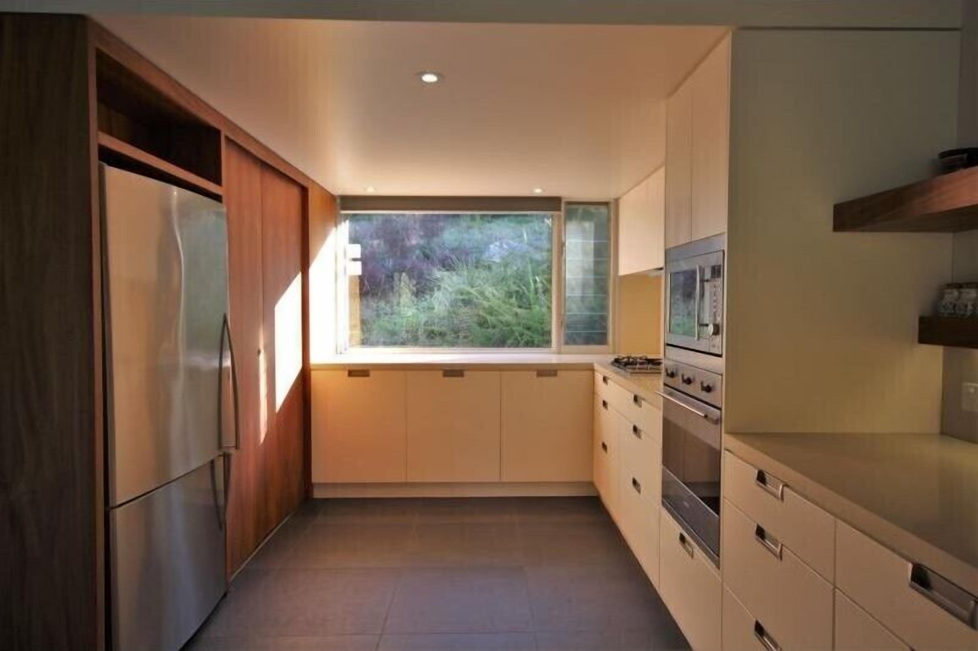 A modern kitchen with built-in appliances, a window with a view of greenery, and a wooden cabinet.
