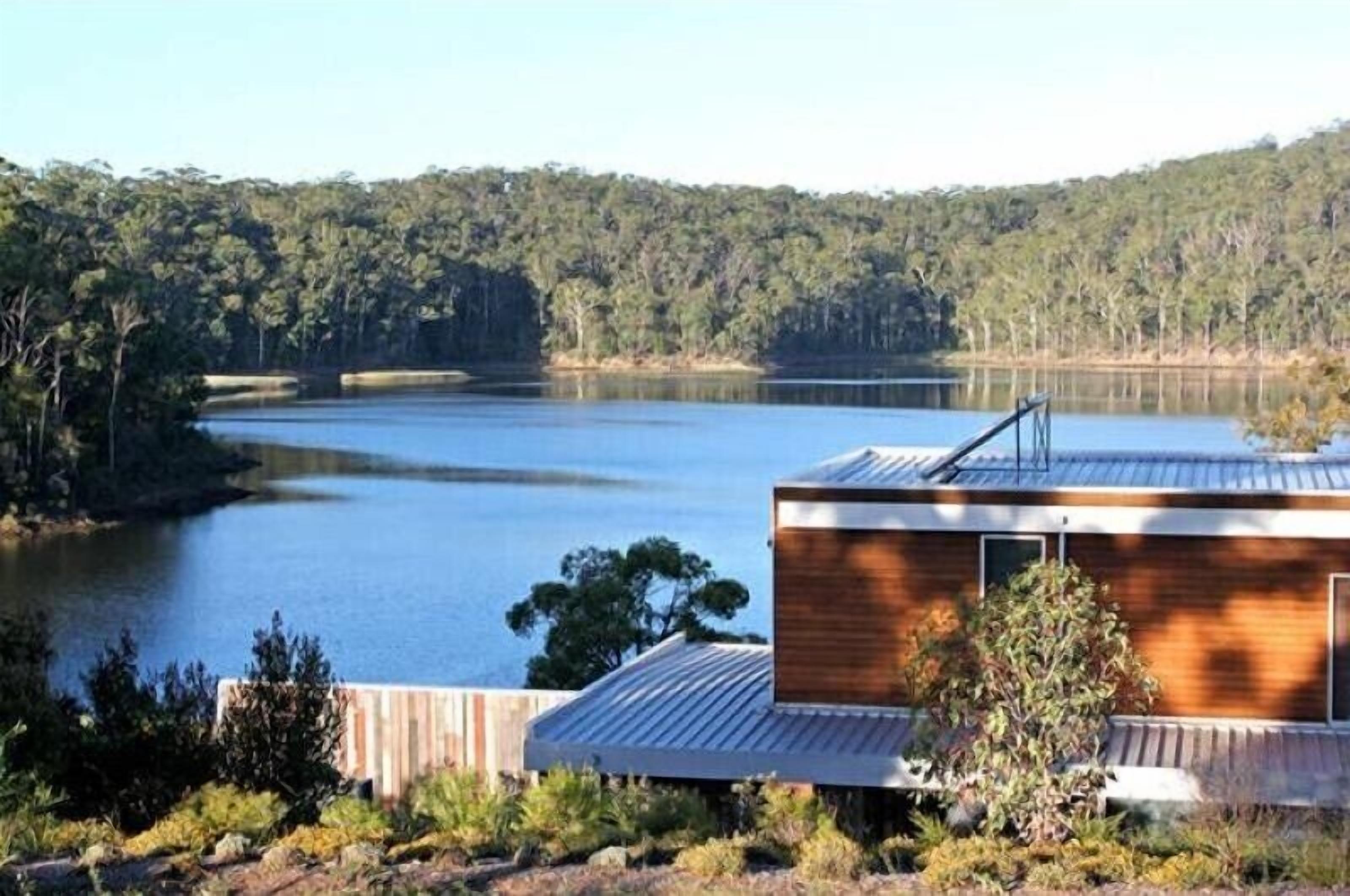 A modern building with a wooden exterior, situated near a lake with dense forest in the background.