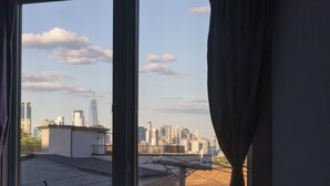 Udsigt gennem et vindue med gardiner, der viser byens skyline med bygninger og en klar himmel.