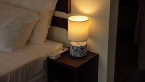 A bed with white linens, a bedside table with a lamp, and a remote control.