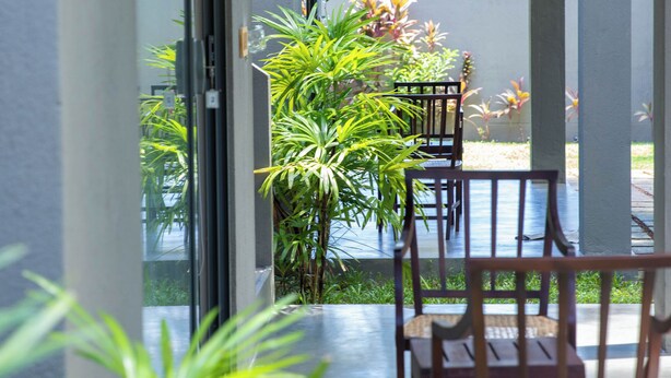 A covered outdoor area with a table and chairs, surrounded by plants and a view of greenery.