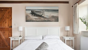 Une chambre à coucher avec un grand lit, deux tables de chevet avec des lampes, une porte en bois et un tableau représentant un bateau accroché au mur.