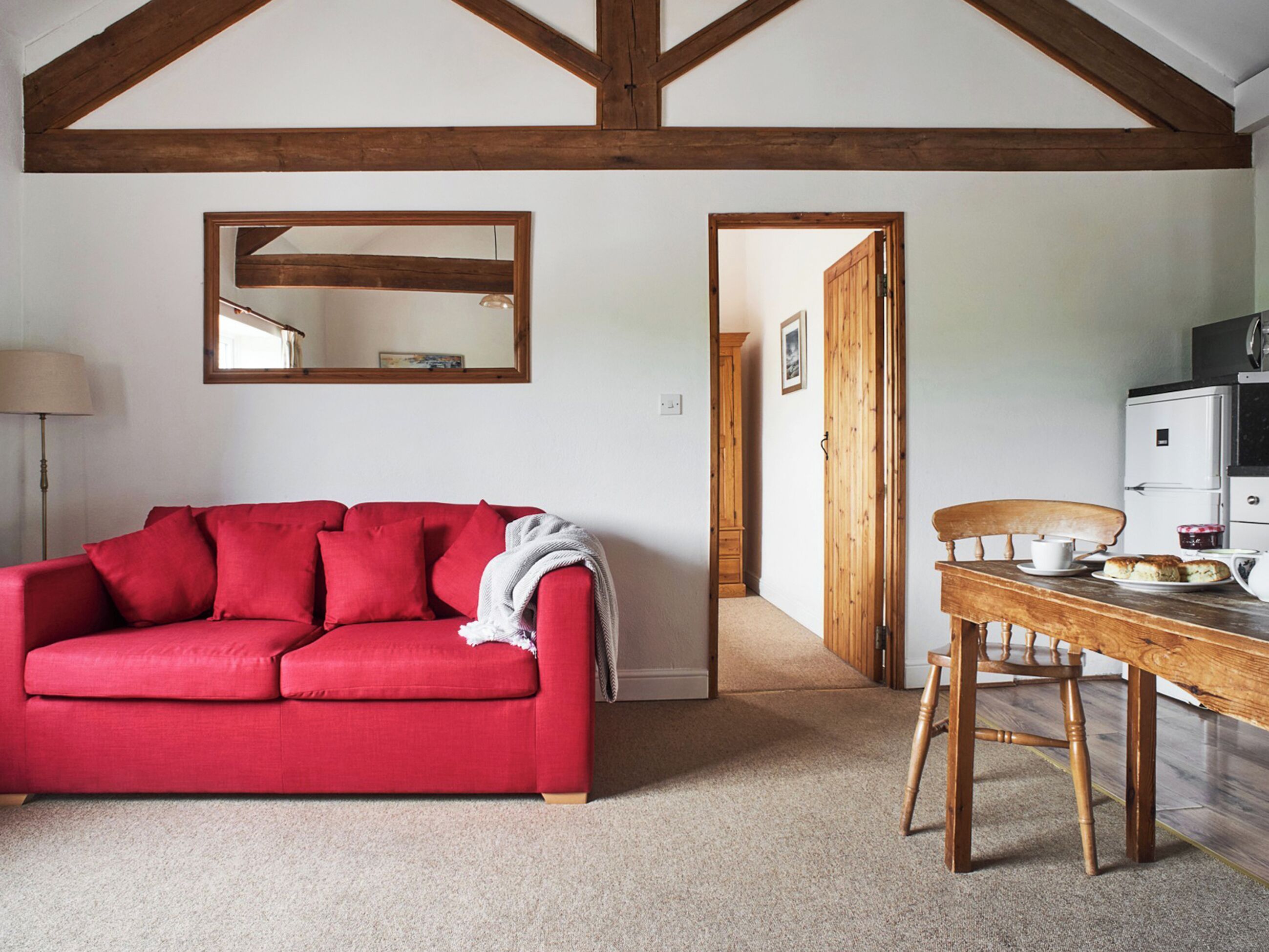 A red sofa, a wooden dining table with chairs, a kitchen area, and a mirror on the wall.