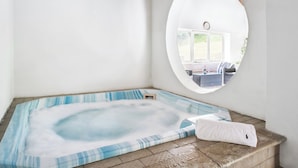Un bain à remous avec vue sur un espace extérieur aménagé, visible à travers une fenêtre circulaire.