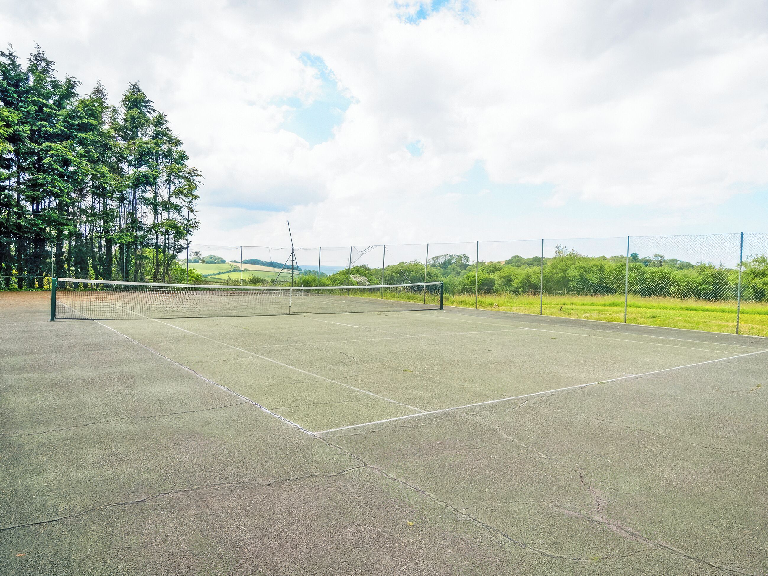 Ein Tennisplatz im Freien mit Netz, umgeben von Bäumen und einem Zaun.
