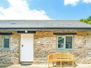 Une petite maison en pierre avec une porte, deux fenêtres et un banc.