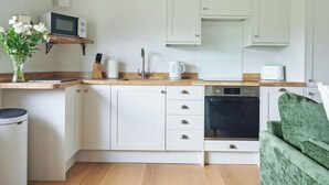 Een kleine keuken met witte kastjes, een magnetron, een waterkoker en een broodrooster.