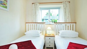 Een slaapkamer met twee bedden, een nachtkastje met een lamp, een raam met gordijnen en een schilderij aan de muur.