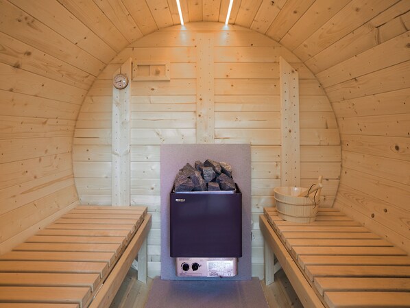 Una sala de sauna con bancos de madera, un calentador de sauna y una pared de madera.