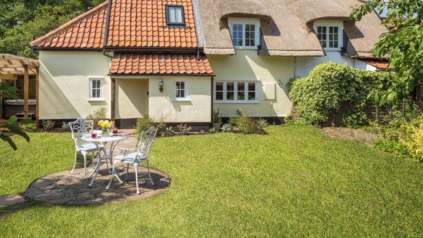 A house with a tiled roof, a thatched roof section, and a garden with a table and chairs.