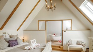 A bedroom with a bed, a chair, a vanity, a mirror, a chandelier, and a skylight.