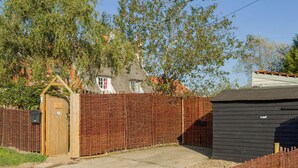 A fenced property with a wooden gate, a shed, and a house with a thatched roof.