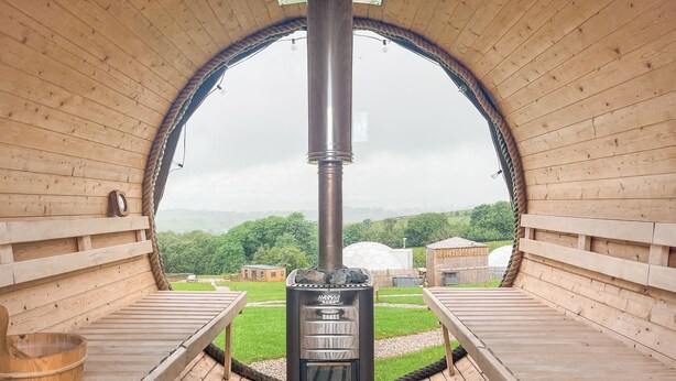 Eine Holzsauna mit einem zentralen Schornstein, Bänken und Blick auf die umliegende Landschaft.
