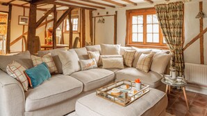 Una sala de estar acogedora con vigas de madera a la vista, un sofá modular y una mesa de centro con una bandeja de pasteles.