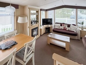 Ein Wohnzimmer mit Holztisch, weißen Stühlen, einer Couch, einem Fernseher und einem Kamin.