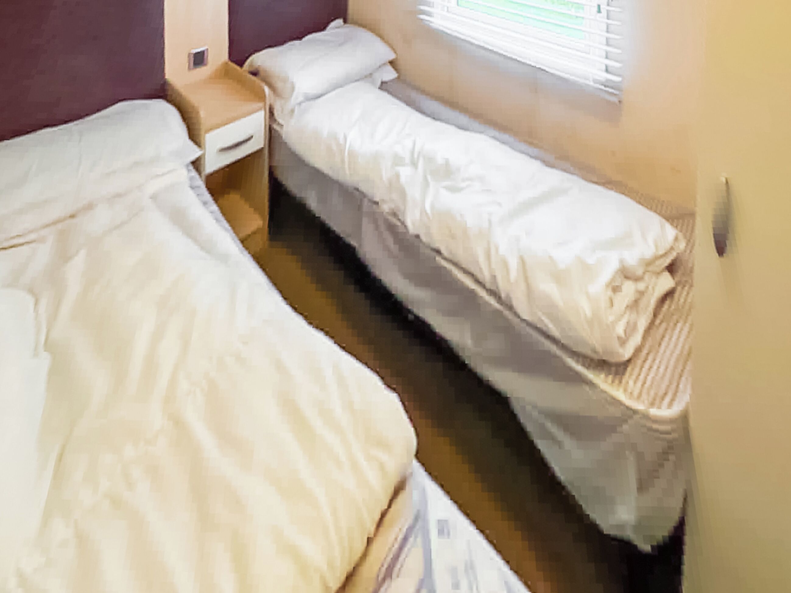 Ein Zimmer mit zwei Einzelbetten, einem Nachttisch und einem Fenster mit Jalousien.