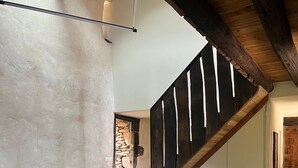 Un interior rústico con una mesa y banco de madera, un muro de piedra y una escalera de madera.