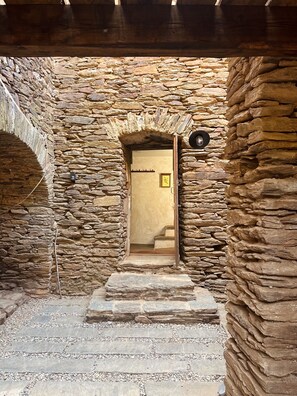 A stone-walled corridor with a wooden door and steps leading to an interior space. - An Ardèche farmhouse at the foot of the Cévennes (Saint-Pierre-Saint-Jean)