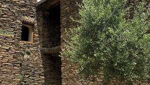 Un edificio de piedra con una ventana pequeña y una puerta, rodeado de grava y un árbol.