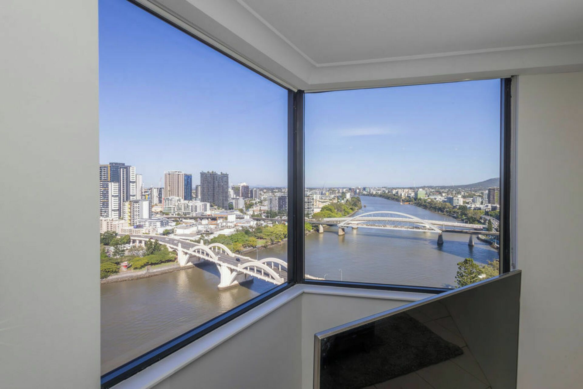 A room with a large window overlooking a cityscape, a river, and a bridge.