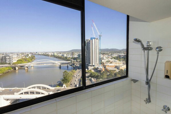 Ein Badezimmer mit großem Fenster und Blick auf eine Stadtlandschaft, einschließlich eines Flusses und einer Brücke.