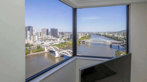 Eine hohe Wohnung mit einem großen Fenster und Blick auf eine Stadtlandschaft, darunter ein Fluss und eine Brücke.