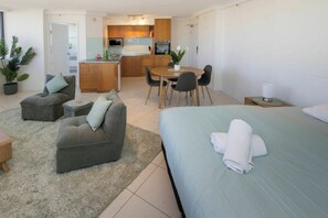 Ein modernes Hotelzimmer mit Bett, einer Couch, einem Esstisch mit Stühlen, einer Küchenzeile und einem kleinen Balkon.
